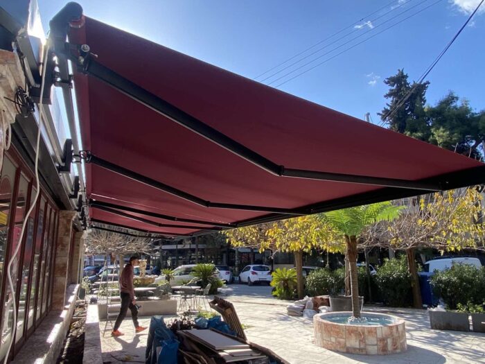 Τεντόπανα σε έντονο μπορντό χρώμα, εξοπλισμένα με σύγχρονο μηχανισμό, ιδανικά για επαγγελματικούς εξωτερικούς χώρους, προσφέροντας προστασία από τον ήλιο και καλαίσθητη εμφάνιση.