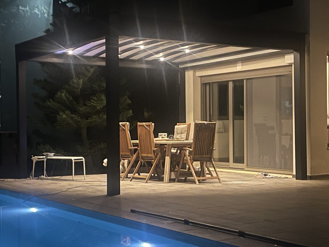Πέργκολα με φωτισμό LED πάνω από τραπεζαρία εξωτερικού χώρου, ιδανική για νυχτερινή χρήση σε κήπους και βεράντες.