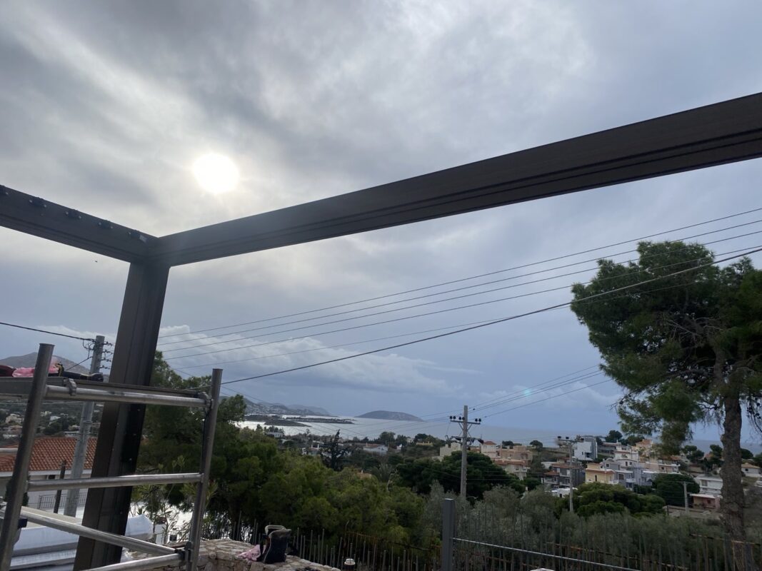 Βιοκλιματική πέργκολα σε στάδιο κατασκευής, με φόντο την εκπληκτική θέα στη θάλασσα και τον ουρανό.