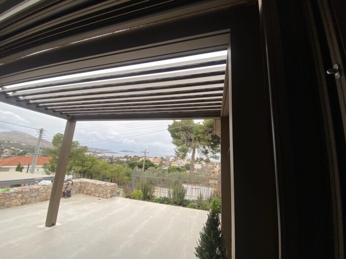 Πέργκολα αλουμινίου με κινητές περσίδες, προσφέροντας ιδανική σκίαση και προστασία, τοποθετημένη σε υπαίθριο χώρο με θέα στη θάλασσα.