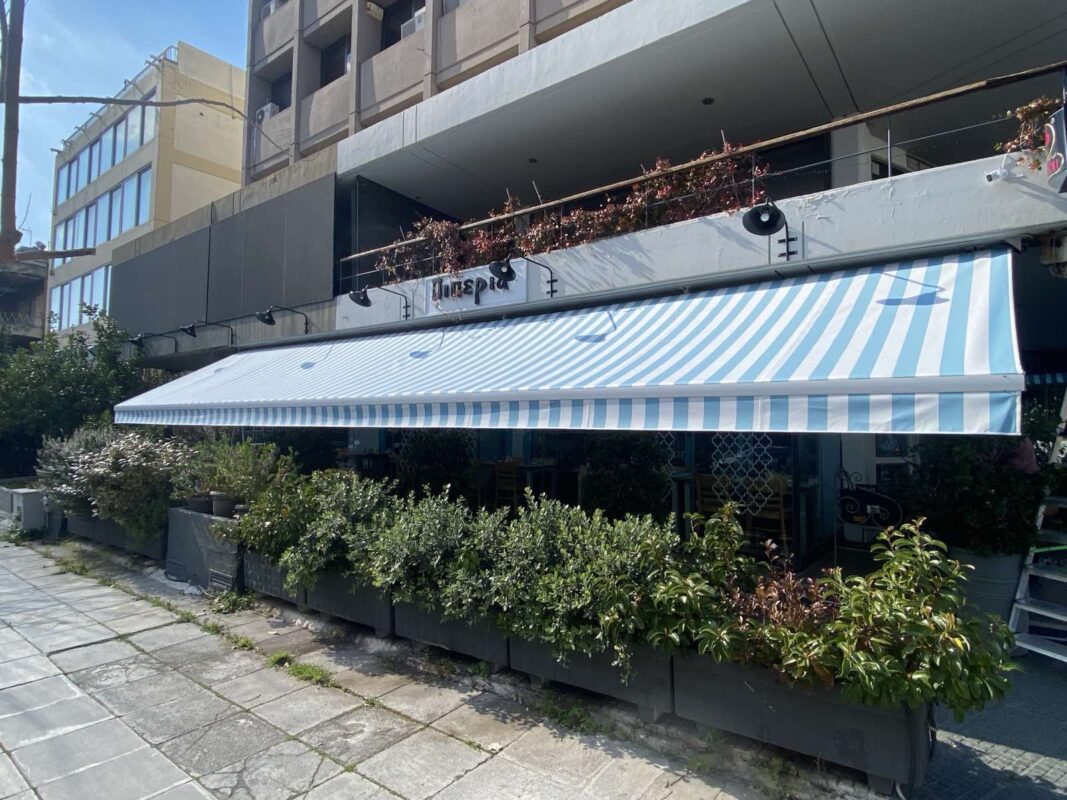 Τέντες σε κατάστημα εστίασης με ριγέ σχέδιο και πλούσια βλάστηση στον εξωτερικό χώρο